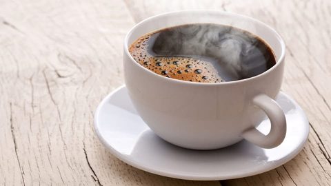 A steaming cup of black coffee on a saucer