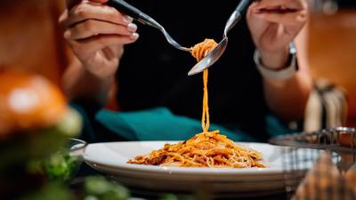 A diner lifting a forkful of spaghetti from a plate in low restaurant light