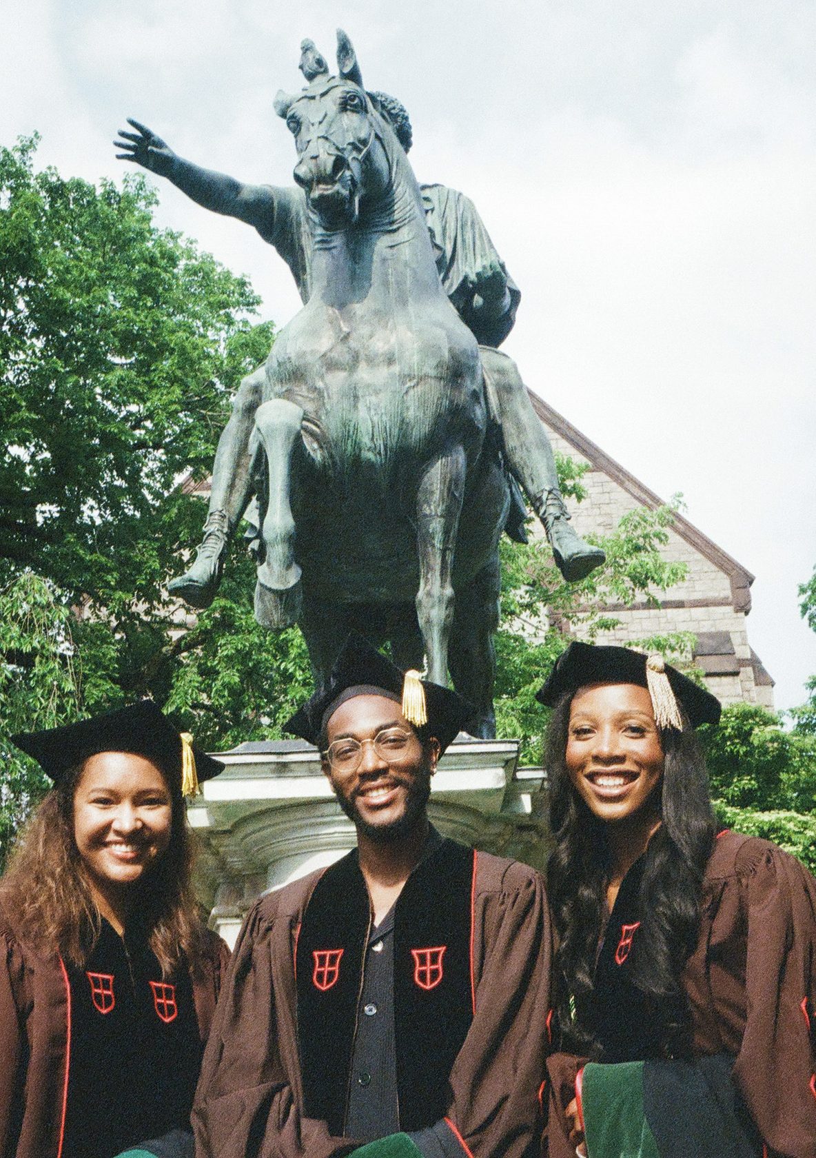 Graduates in caps and gowns posing beside an equestrian statue