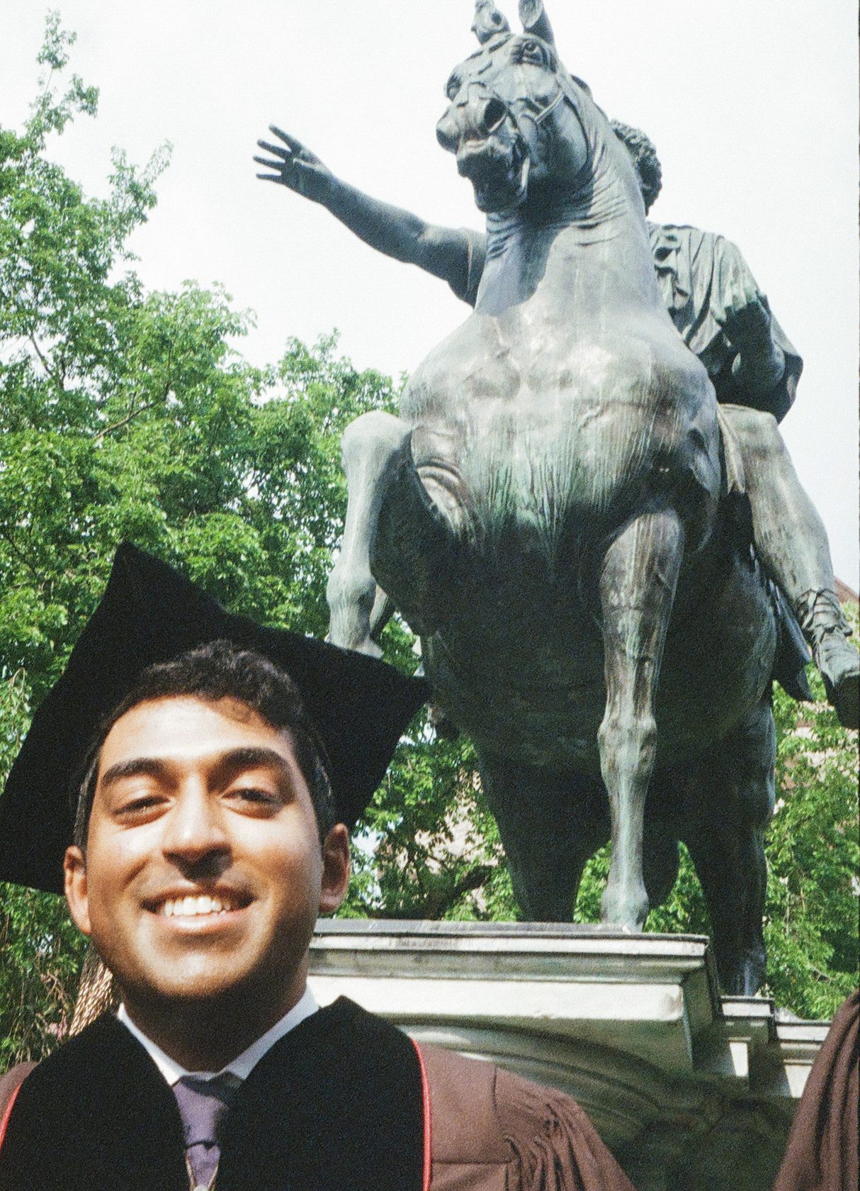 A graduate in cap and gown beside an equestrian statue