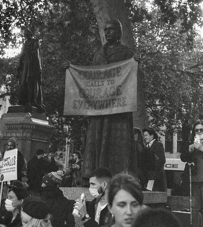 Black and white documentary photograph of a street demonstration with a banner