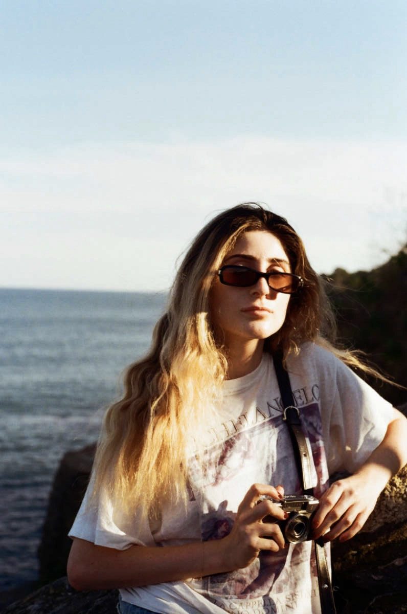 A woman with a camera standing by the water at sunset
